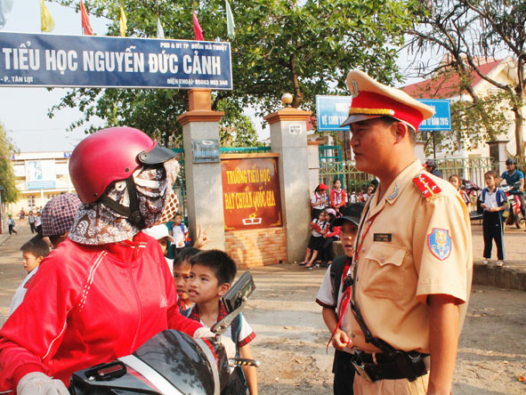Nhắc nhở phụ huynh đội mũ bảo hiểm cho con em mình khi ngồi trên xe  gắn máy tại Trường Tiểu học Nguyễn Đức Cảnh (TP. Buôn Ma Thuột).