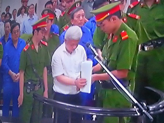 Bị cáo Nguyễn Đức Kiên được cảnh sát áp giải tháo còng trước khi nghe tòa tuyên án - Ảnh chụp qua màn hình
